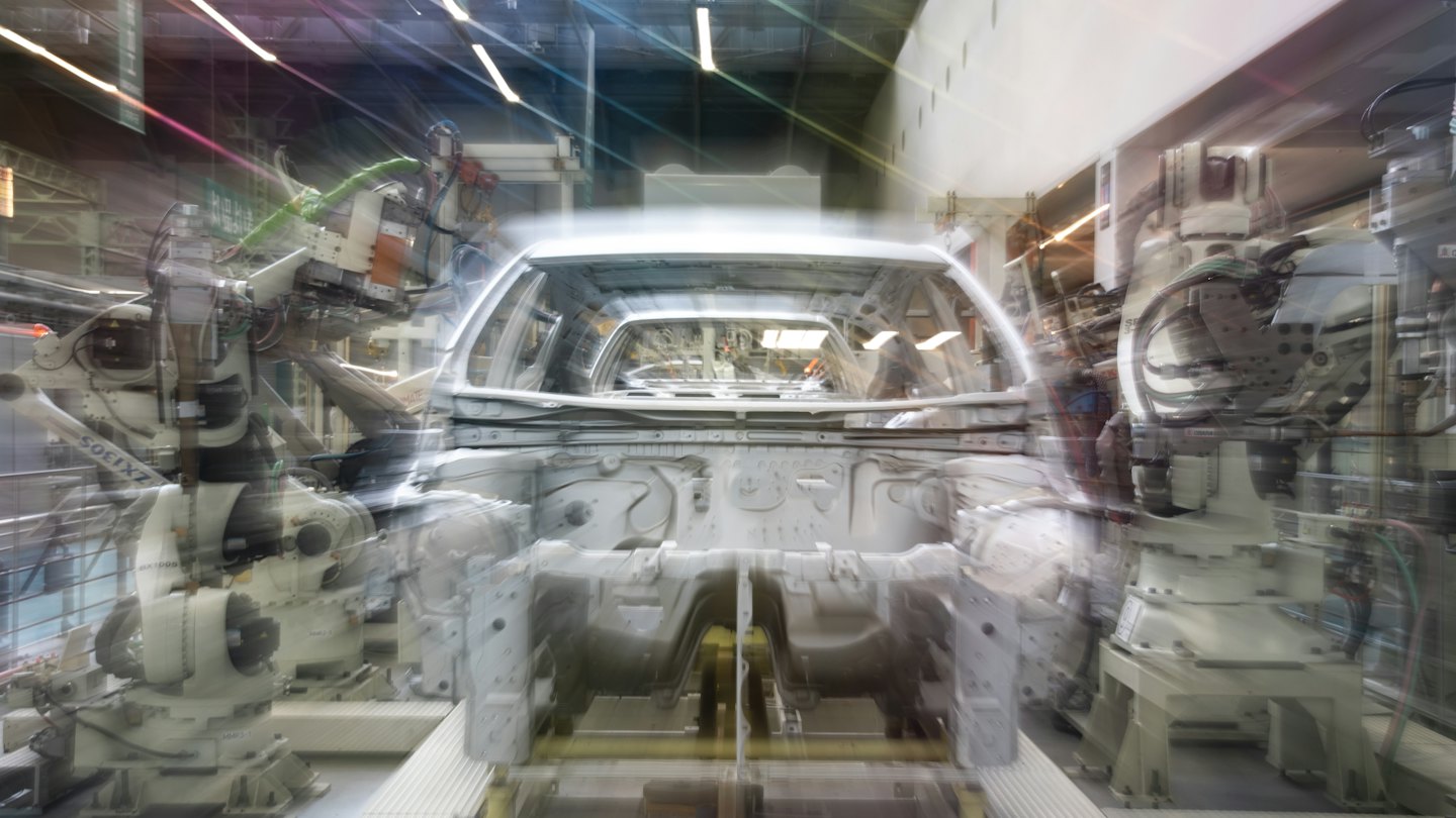 Robotic arms assemble an unpainted car chassis on a factory line.