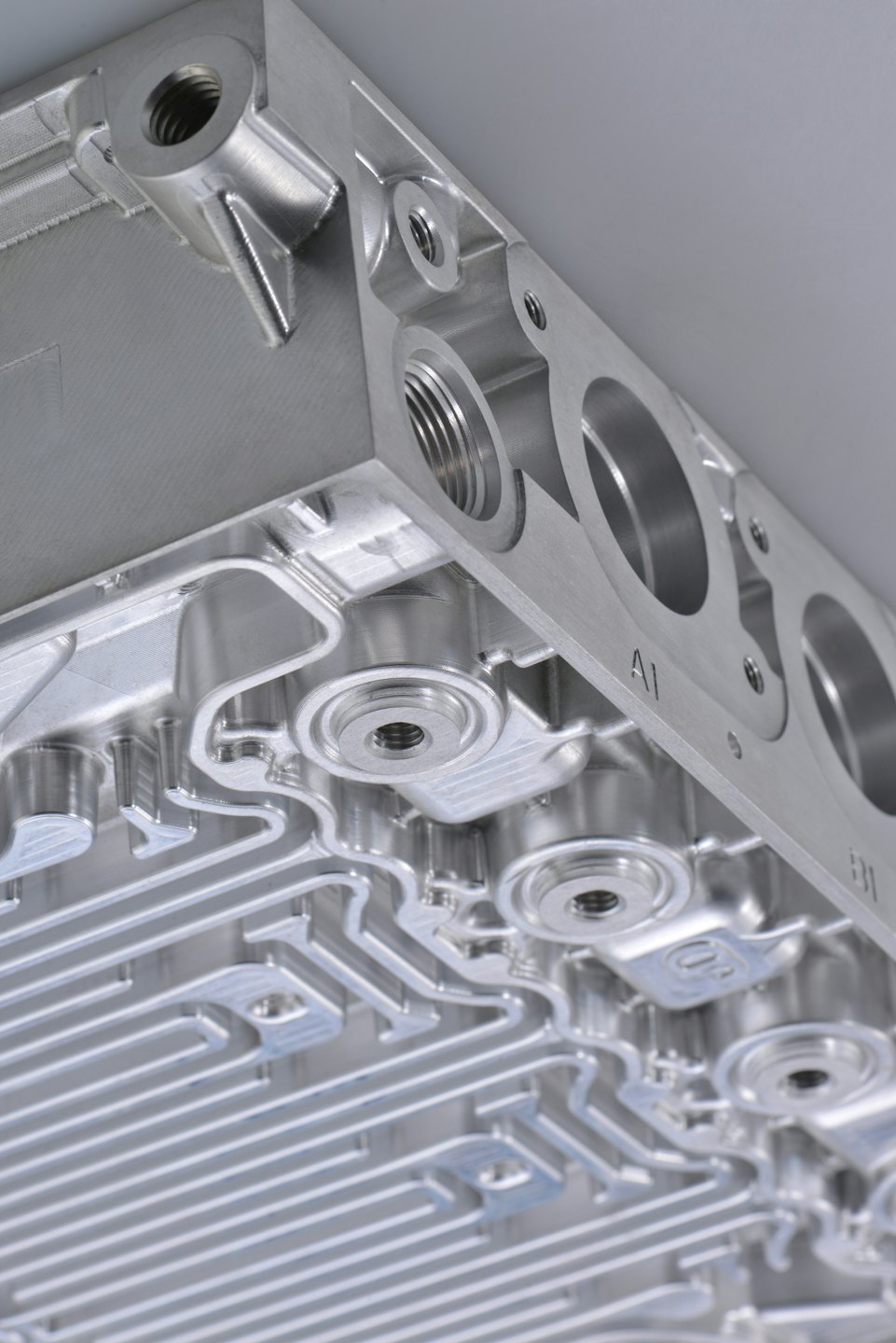 Precisely machined silver metal component with intricate channels and threaded holes.